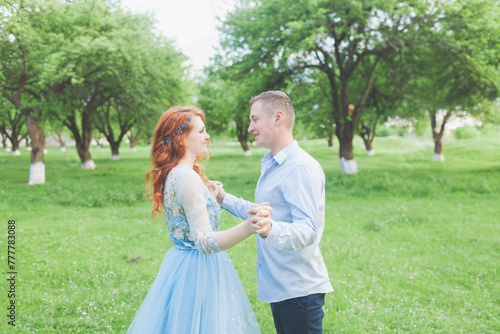 young couple in love are spinning. woman with fiery hair in a blue dress. photo shoot in an apple orchard