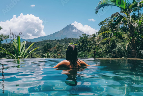 Fototapeta Naklejka Na Ścianę i Meble -  Female Tourist at a luxury tropical hotel pool on a sunny day in Costa Rica looking at a Volcano while on vacation.