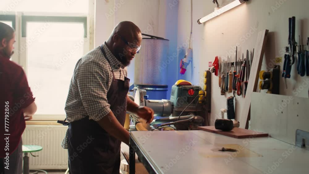 African american man in woodworking shop inspecting lumber piece before assembling furniture, checking for scratches. Cabinetmaker evaluates timber block, ensuring it meets quality standards, camera B African american man in woodworking shop inspecting lumber piece before assembling furniture, checking for scratches. Cabinetmaker evaluates timber block, ensuring it meets quality standards, camera B