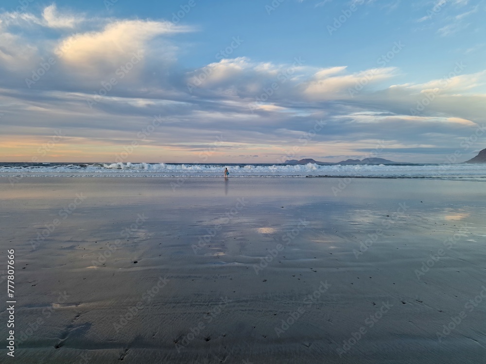 Sunset on Famara Beach, Lanzarote, casts a mesmerizing palette of colors across the sky, blending hues of orange, pink, and purple against the backdrop of the Atlantic Ocean waves.