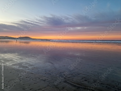 Sunset on Famara Beach  Lanzarote  casts a mesmerizing palette of colors across the sky  blending hues of orange  pink  and purple against the backdrop of the Atlantic Ocean waves.