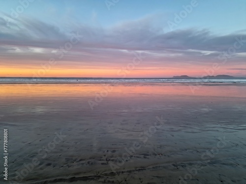 Sunset on Famara Beach  Lanzarote  casts a mesmerizing palette of colors across the sky  blending hues of orange  pink  and purple against the backdrop of the Atlantic Ocean waves.