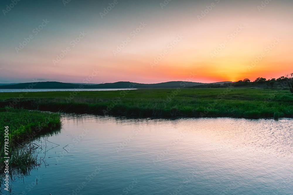 A small picturesque river among a green meadow during sunset. Small river in the countryside. Feeling of freedom, happiness, nostalgia. Tavrichanka, Primorsky Krai, Russia