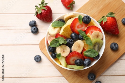 Schilderij op canvas Tasty fruit salad in bowl and ingredients on wooden table, flat lay