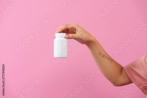 A woman hands delicately hold a bottle of medicine, isolated against pink background, depicting care, health, and the importance of pharmaceutical treatment in healthcare.