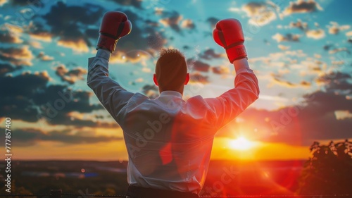 Businessman with boxing gloves victorious - A victorious man in a suit with his hands up, wearing boxing gloves against a sunset, success, triumph, winning, celebration, determination, business, victo