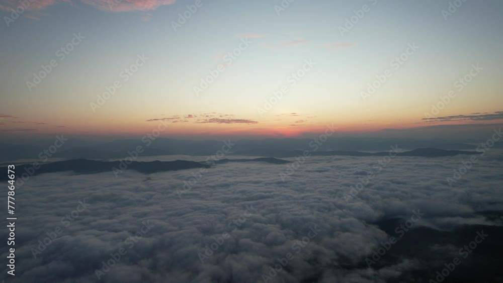 Beautiful aerial view of mountain peak with green trees in fog. Landscape with high rocks, forest, sky. Top view from drone of mountain valley in low clouds. Beautiful aerial view of mountain peak with green trees in fog. Landscape with high rocks, forest, sky. Top view from drone of mountain valley in low clouds.