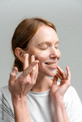 A woman applies cream to her face