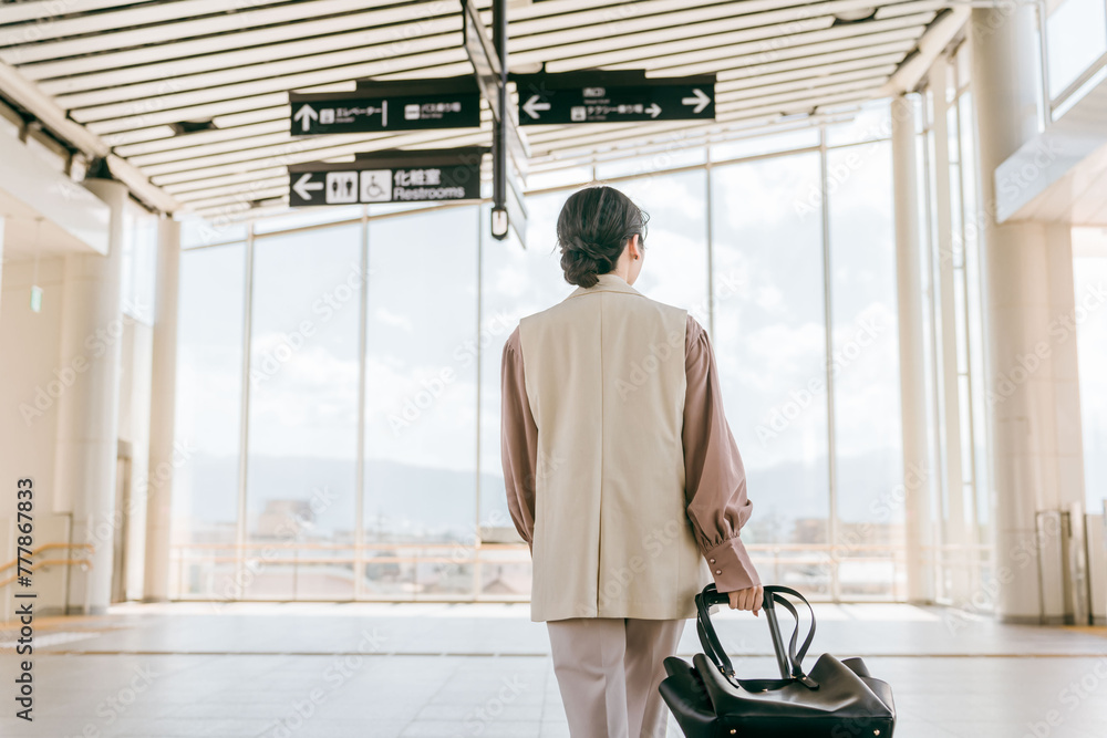 空港・駅・ビル・公共交通施設でスーツケースを持って歩くビジネスウーマン（海外出張・徒歩）
