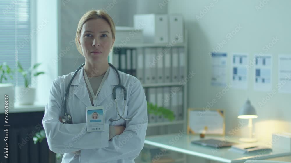 Confident female physician in white coat with stethoscope over neck posing at camera with arms crossed in clinic. Video portrait, copy space Confident female physician in white coat with stethoscope over neck posing at camera with arms crossed in clinic. Video portrait, copy space