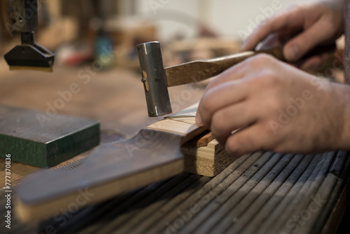 Luthier puts the frets on the guitar neck photo