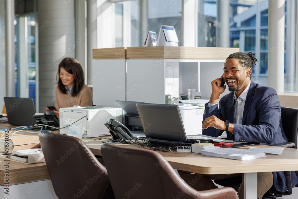 Smiling businessman talking on mobile phone while working at office Smiling businessman talking on mobile phone while working at office