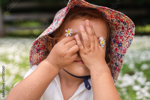 Toddler using daisies flower to replace her eyes photo