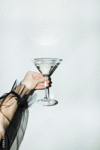 Hand with elegant ruffled mesh shirt holding martini glass with drink