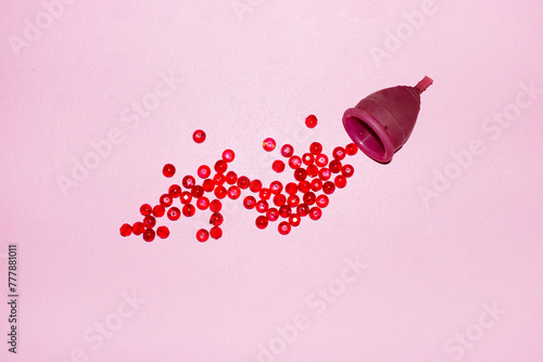 Conceptual period photo of period cup and red pearls as blood photo