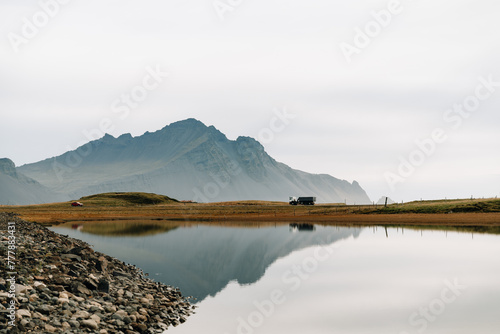 Mountain peak, winding track, SUV reflected in water by rocky coast