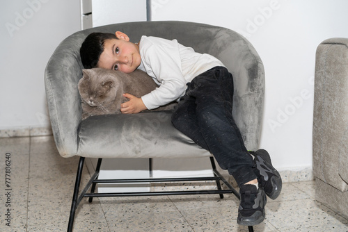 Portrait Happy Boy Cuddling Cat on Modern Armchair With Flash Light.