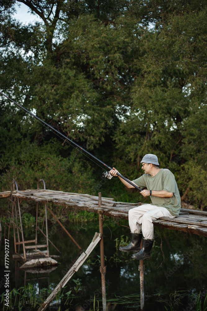 Fisherman with fishing rod on a footbridge near the lake at summer Fisherman with fishing rod on a footbridge near the lake at summer