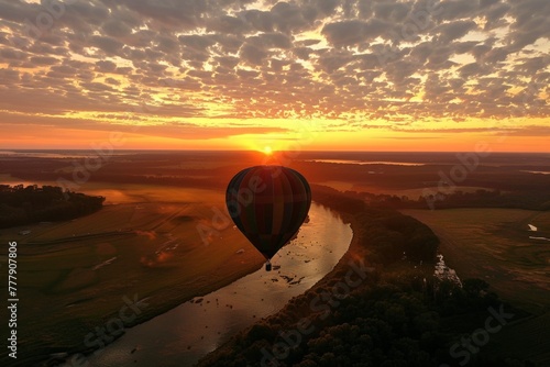 Aerial perspective of a hot air balloon silhouetted against a breathtaking sunset, floating over a scenic landscape