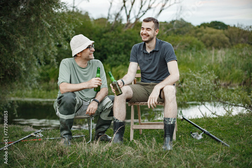 Two fishermen with fishing rods drinking a beer near the lake