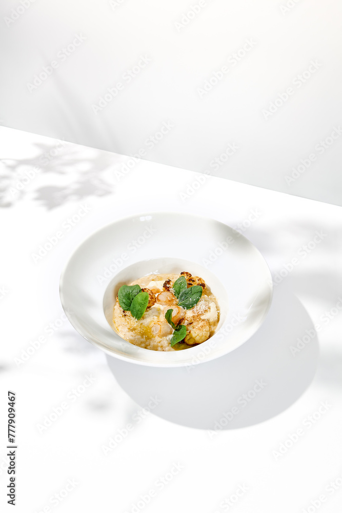 Seafood risotto with scallops and cauliflowers on white plate. Creamy risotto with sea scallops and cauliflowers. Italian risotto with sea scallops on light background with shadows of leaves Seafood risotto with scallops and cauliflowers on white plate. Creamy risotto with sea scallops and cauliflowers. Italian risotto with sea scallops on light background with shadows of leaves