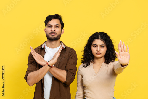 Young man and woman making stop gestures against a yellow background, expressing denial and boundaries with serious faces.