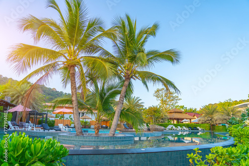 Beautiful outdoor tropical nature landscape of swimming pool in hotel resort with coconut palm tree umbrella and chair nearly sea ocean beach at sunrise time.