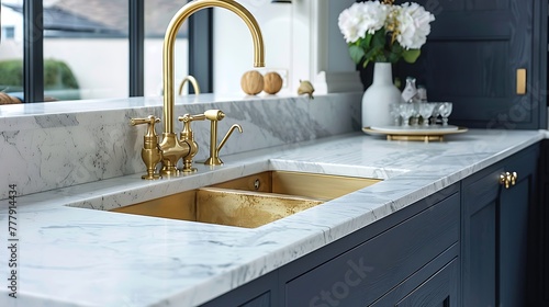 showing a gold sink with gold single lever monobloc tap inset in white marble kitchen counter over navy wood grain effect floor cabinets