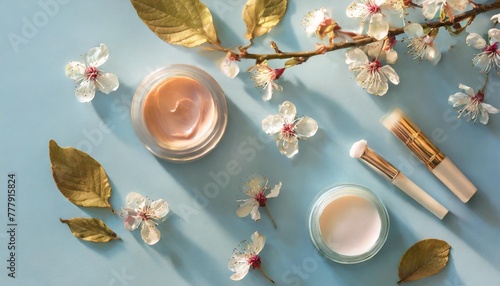 beauty background with facial cosmetic products leaves and cherry blossom on pastel blue desktop background modern spring skin care layout top view flat lay