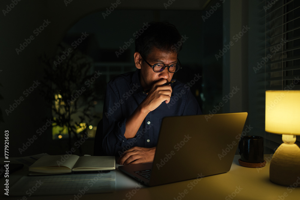 Serious businessman sitting at desk and working late at night . Serious businessman sitting at desk and working late at night .