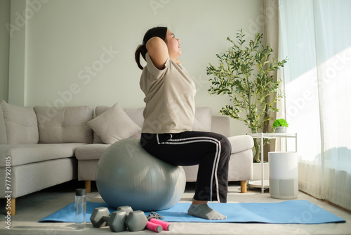 Full length of young overweight woman exercising with fitness ball on mat at home. Healthy lifestyle concept.