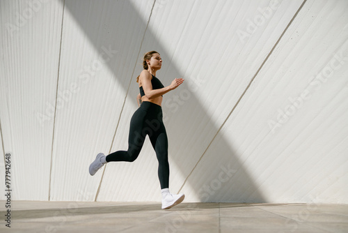 Active woman athlete is jogging on morning on modern building background. Healthy life concept