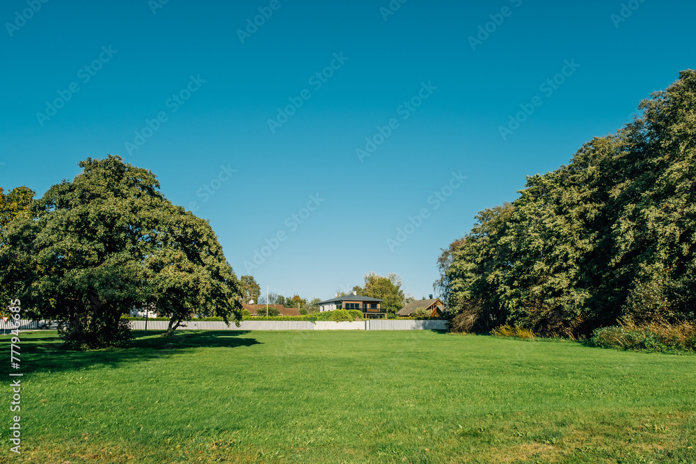 Scenic summertime view of a beautiful english style landscape with a green lawn, leafy trees and house