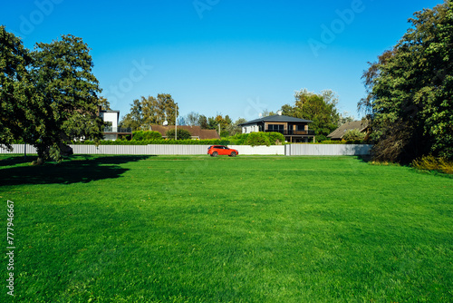 Scenic summertime view of a beautiful english style landscape with a green lawn, leafy trees and house