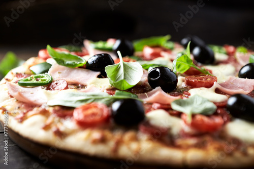 Pizza with ham, mozzarella cheese, cherry tomatoes, green and jalapeno pepper, black olives and fresh basil. Dark background. Close up.