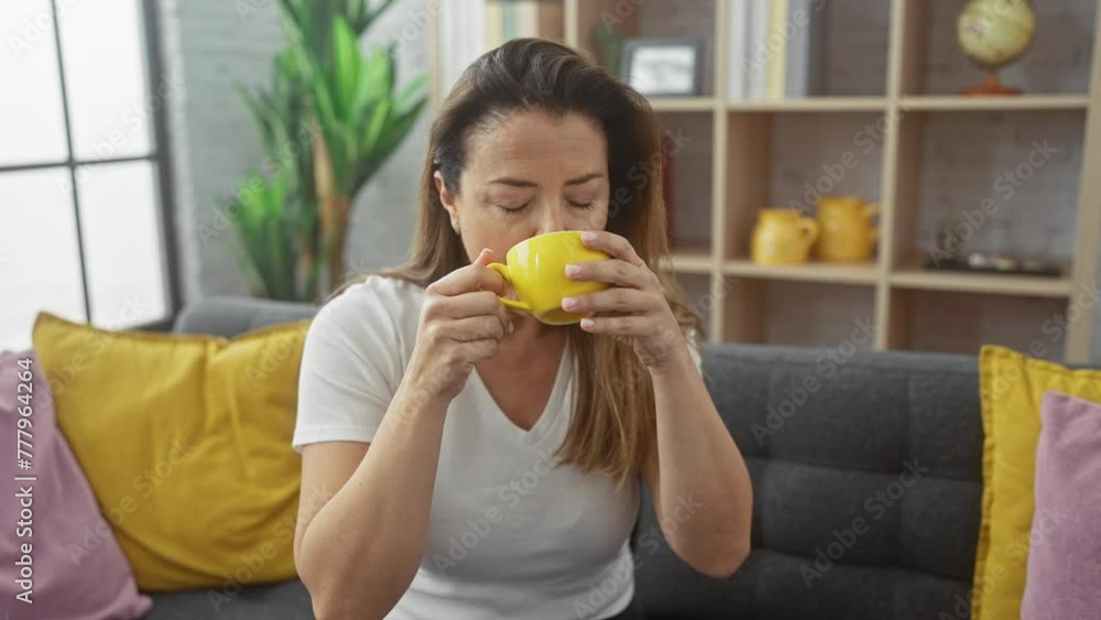 A serene hispanic woman enjoying a cup of tea in a cozy, modern living room with colorful pillows and decor. A serene hispanic woman enjoying a cup of tea in a cozy, modern living room with colorful pillows and decor.