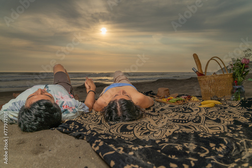 Couple in love at a picnic, lying looking at the sky on the beach