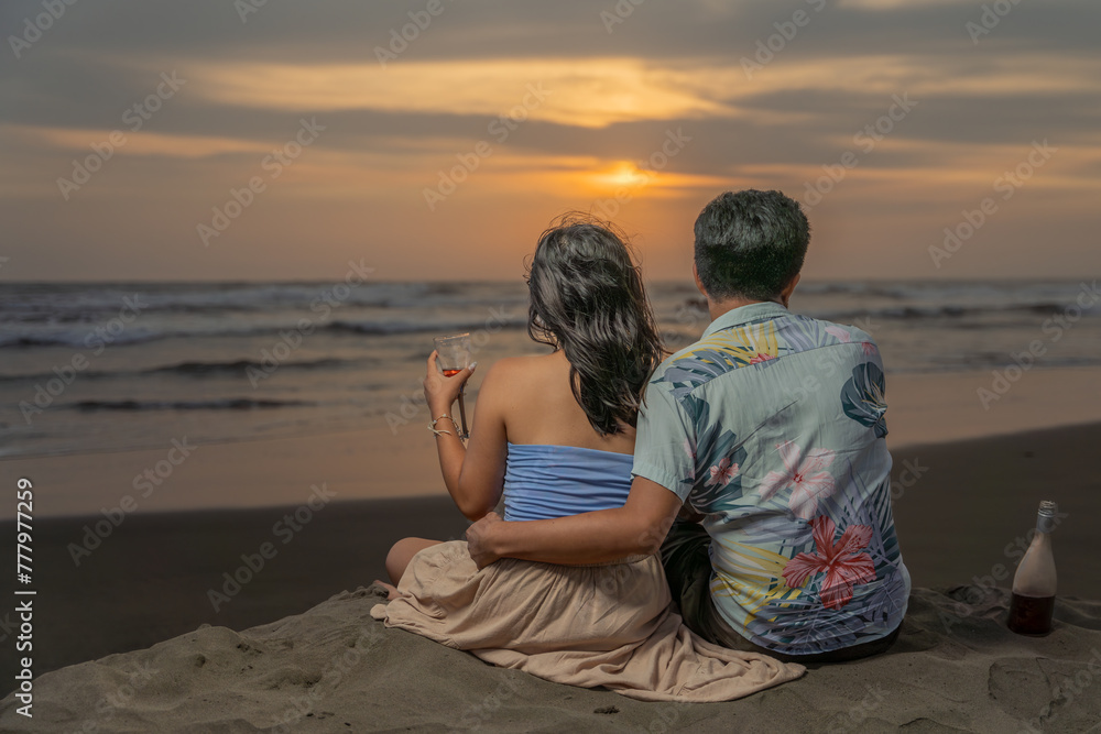 Fototapeta premium Couple in love embracing, toasting with wine, looking at the sea at sunset