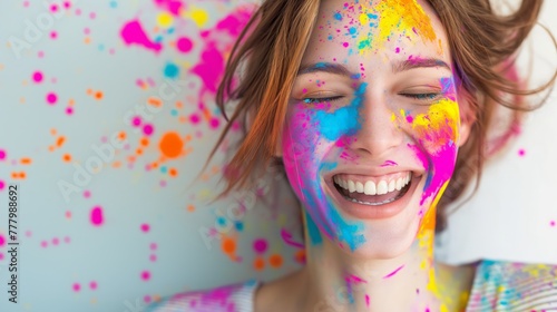Laughing woman with colorful paint splashes on face, representing joy and creative expression.