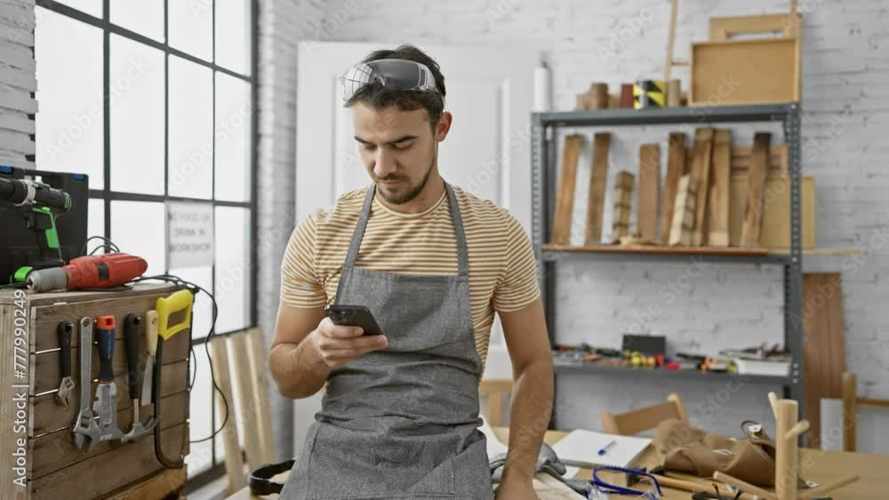 Handsome young man texting on smartphone in a well-equipped carpentry workshop Handsome young man texting on smartphone in a well-equipped carpentry workshop