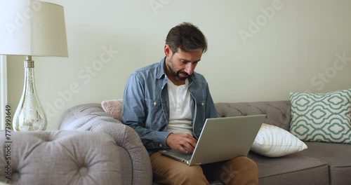 Wallpaper Mural Serious mature Portuguese man working on laptop seated on sofa in living room, busy in teleworking workflow, typing e-mail, solve business remotely, lead correspondence by messaging use modern device Torontodigital.ca