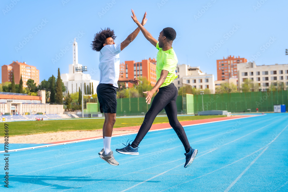 African american young runners jumping high-fiving in a running track