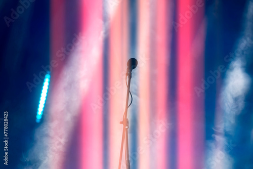 A concert microphone against a background of multicolored light and smoke from the stage spotlights.