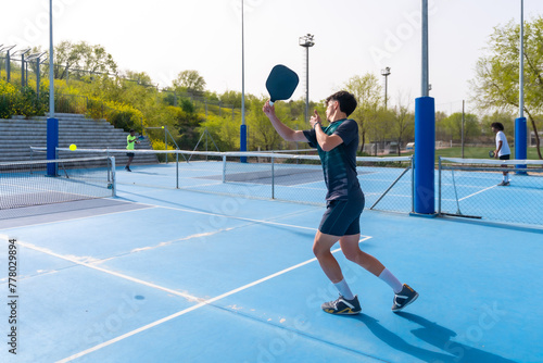 Sportive young man playing pickleball in an outdoor blue court