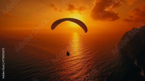 A man is flying a parachute over the ocean at sunset. The sky is orange and the water is calm