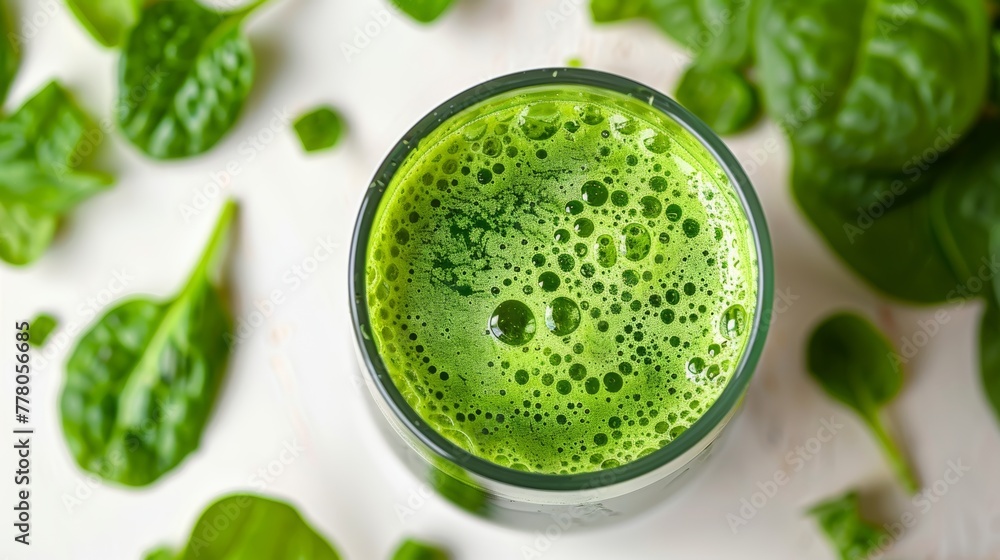 Freshly blended green juice in a glass surrounded by spinach leaves Freshly blended green juice in a glass surrounded by spinach leaves