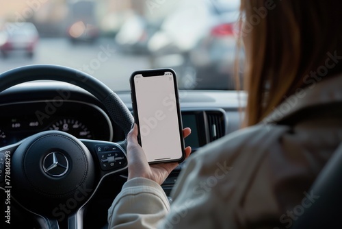 Woman sitting behind the wheel and showing phone with white screen mockup through window