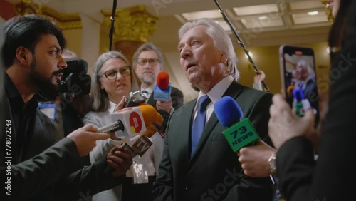 Politician answers press questions and gives interview on television political program. Senior diplomat surrounded by crowd of journalists in government building. Press conference. Hot button issues. photo