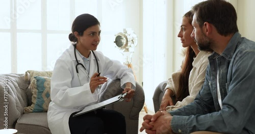 Indian woman fertility specialist in uniform provide consultation, explain treatment plan to young childless Portuguese couple during visit in private clinic. Infertility, professional medical service photo