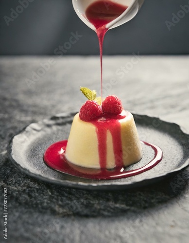 A vivid red raspberry coulis being artfully drizzled over a vanilla panna cotta, set on a sleek, dark stone countertop, highlighting the contrast of colorы